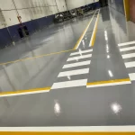 Área de circulação com piso epóxi cinza, faixas de pedestres e demarcação amarela