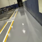 Corredor com piso epóxi cinza, faixas amarelas e faixa de pedestres