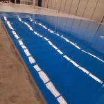 Piso epóxi azul aplicado em etapas ao lado do concreto em galpão