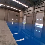 Piso epóxi azul aplicado ao lado de área de concreto em galpão logístico