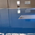 Piso epóxi azul recém-aplicado em galpão, ao lado de faixa de concreto