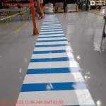 Faixa de pedestres azul e branca em corredor industrial