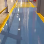 Piso epóxi azul com faixas amarelas refletindo a iluminação