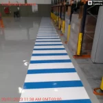 Faixa de pedestres azul e branca em piso epóxi cinza