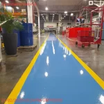 Corredor de fábrica com faixa de circulação em epóxi azul e bordas amarelas