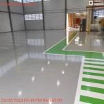 Piso epóxi cinza com faixa verde de circulação e faixa de pedestres