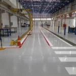 Piso epóxi cinza com faixas de pedestres brancas em linha de produção