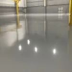 Piso epóxi cinza claro brilhante com pilares amarelos ao fundo
