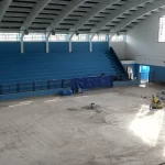 Ginásio com arquibancada azul e piso em preparação